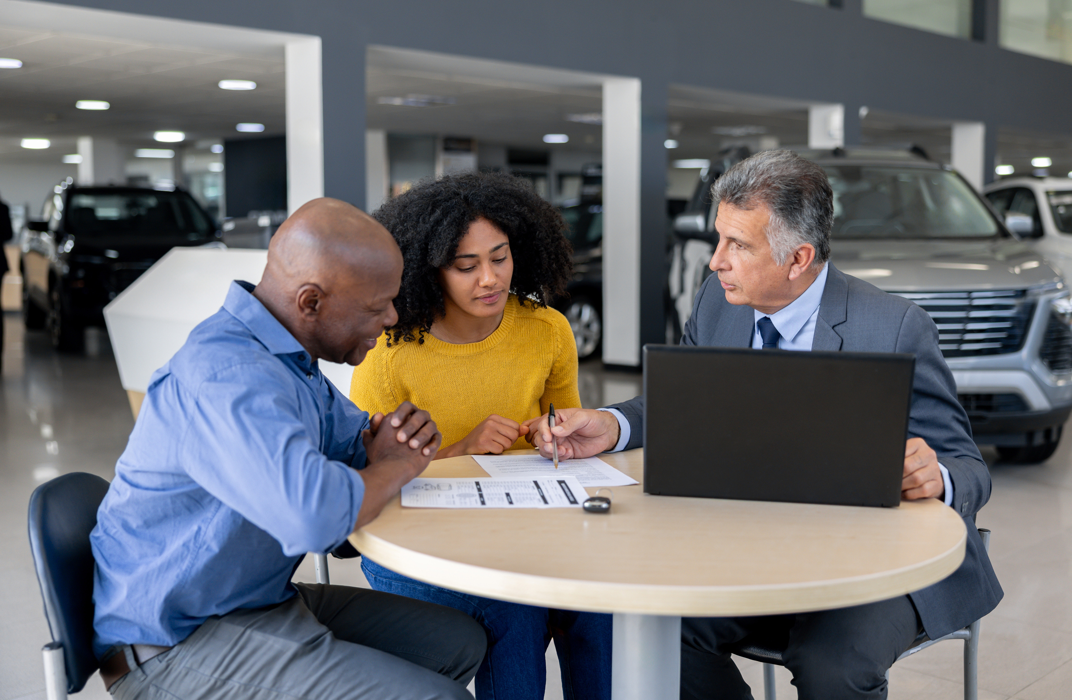 A car salesman explains a vehicle service contract to a couple at a dealership.