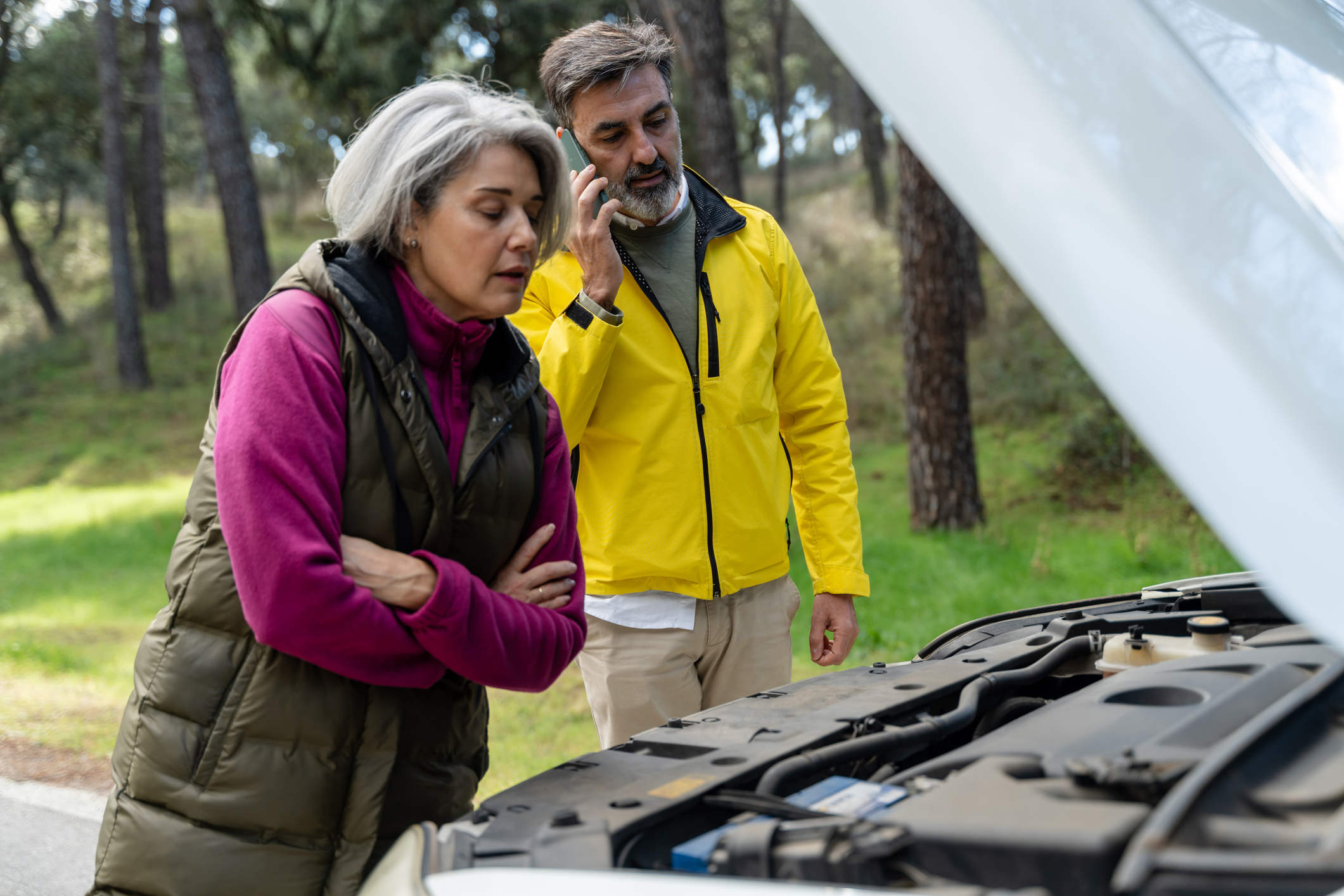 A couple looks at their car's engine after a breakdown on the side of the road.