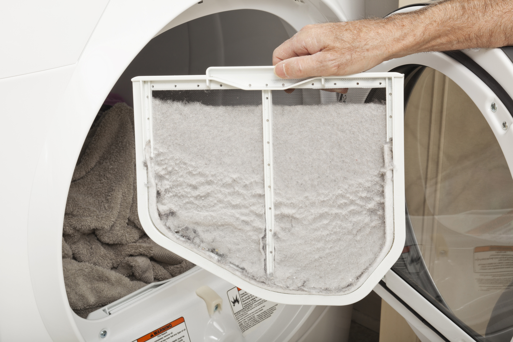 A close-up of a person holding a dryer lint filter heavily coated in gray lint.
