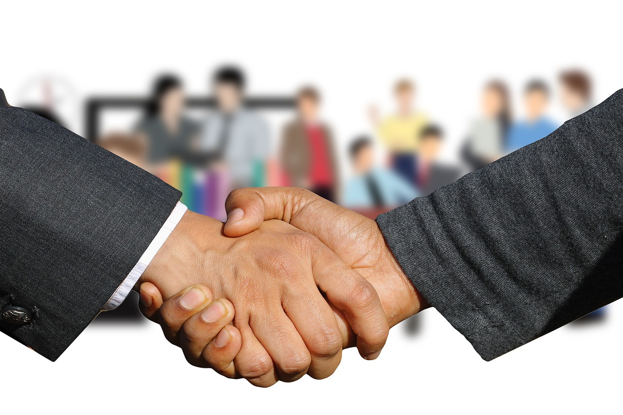 Two business professionals shaking hands over a table with tablets and financial reports.
