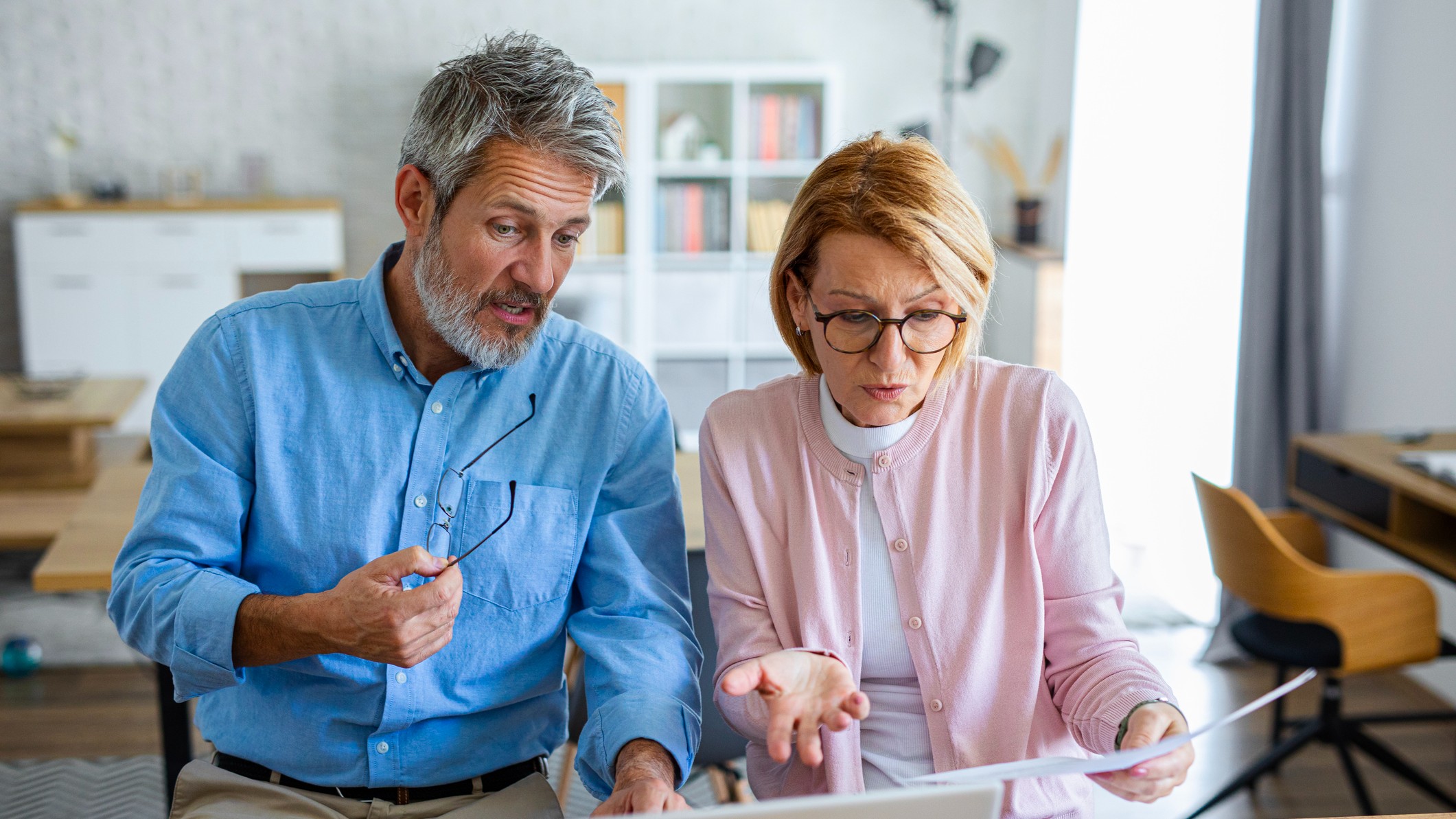 An older couple looking stressed while reviewing financial documents and a laptop at home.