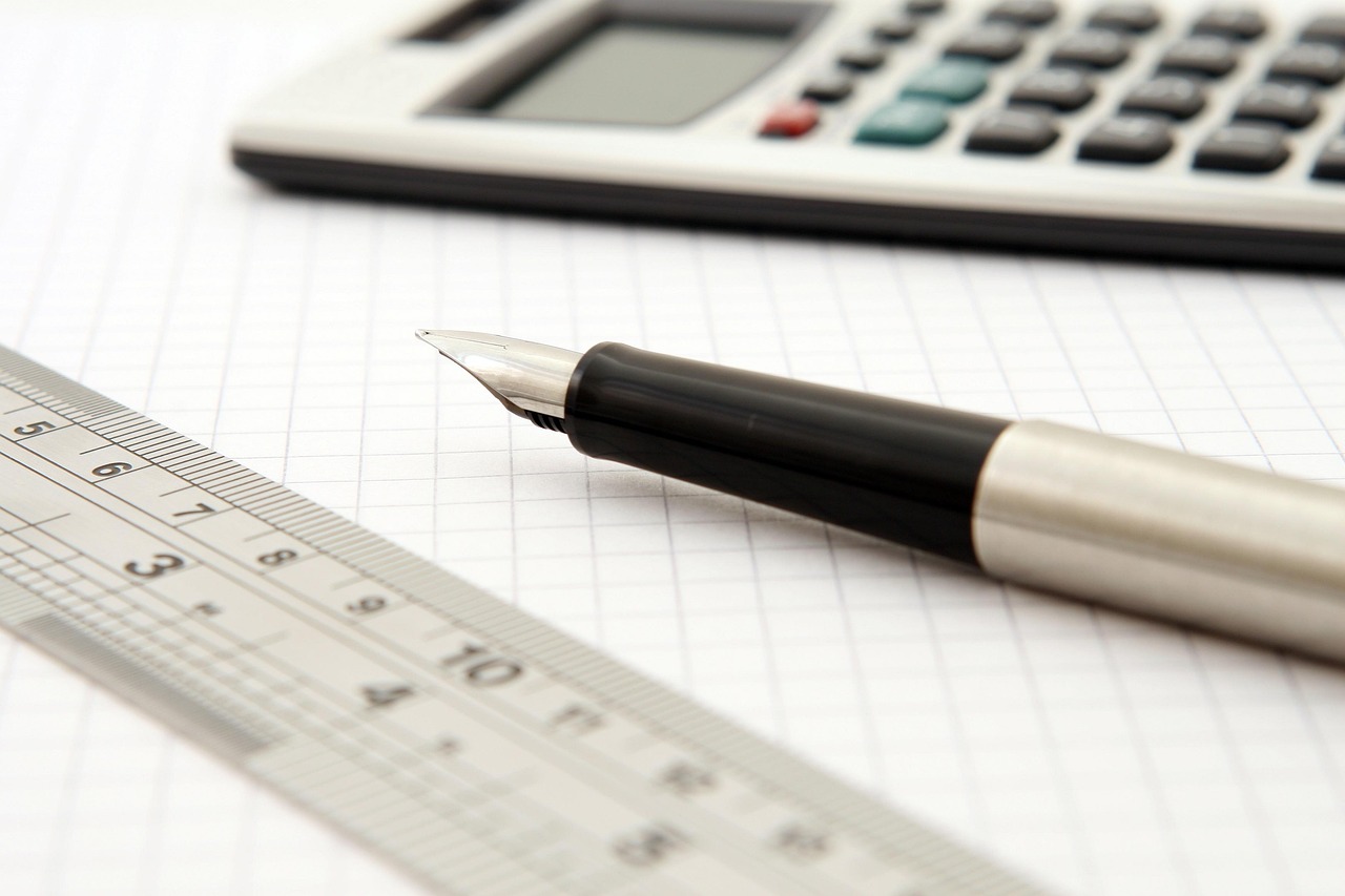 A clean workspace featuring a calculator, a pen, and an open notebook with financial data.