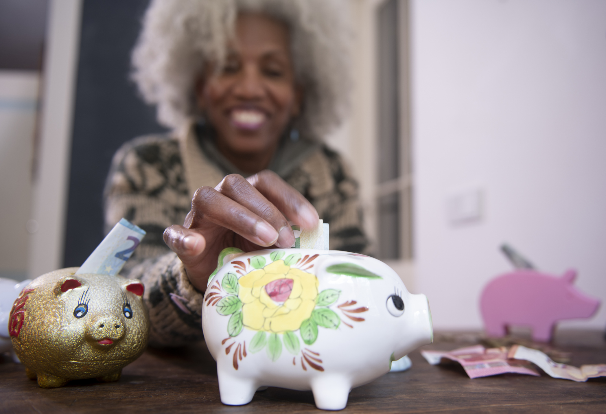 A woman putting dollar bills into a floral piggy bank.