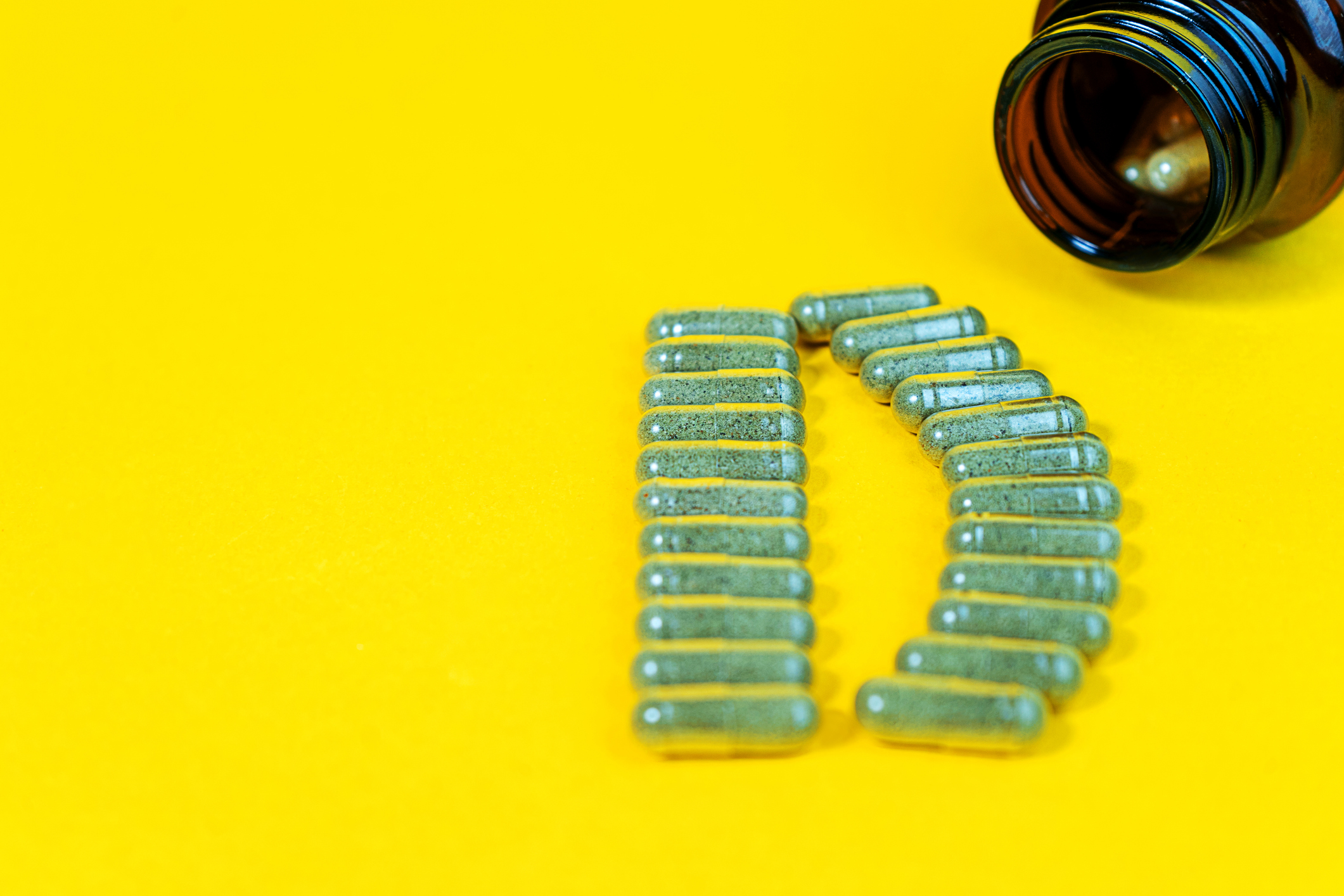 Yellow pills forming the shape of the letter D next to a vitamin bottle.