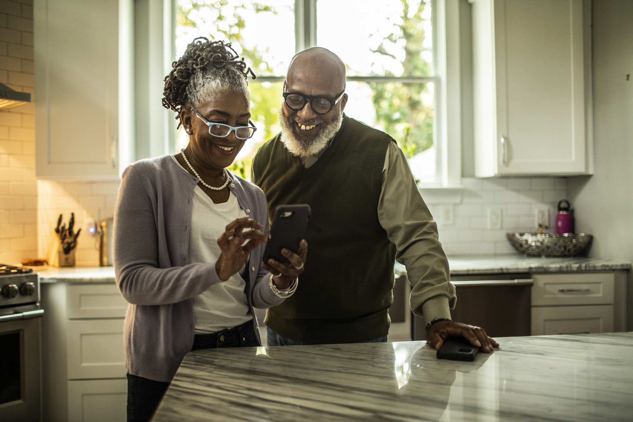A senior couple using a smartphone together in their kitchen.