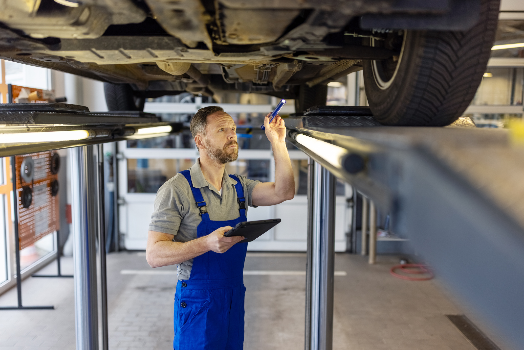 A mechanic inspecting a car's undercarriage in a well-equipped repair shop.