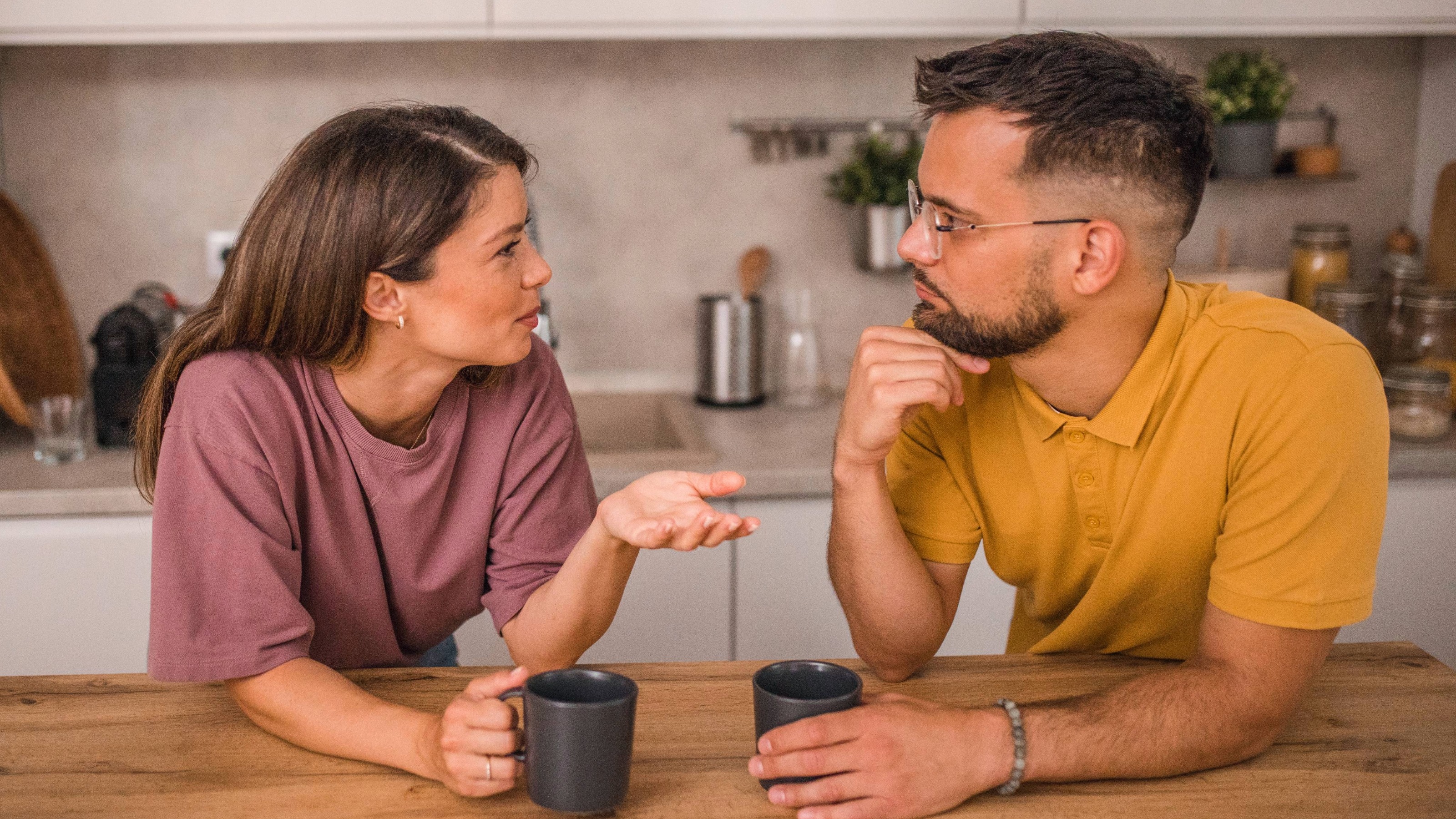 A couple engaged in a positive conversation while drinking coffee at a kitchen counter.