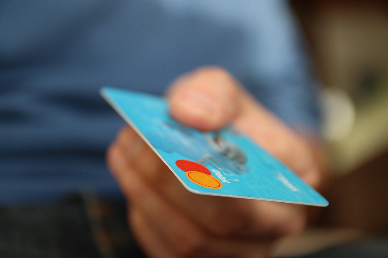 A person using a laptop and a debit card for online banking in a bright cafe.